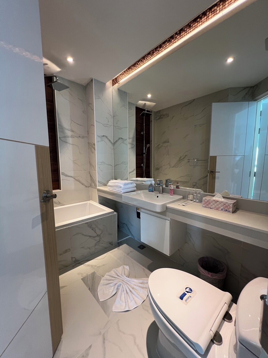 Un baño moderno con piso de mármol, un espejo grande, ducha y retrete.