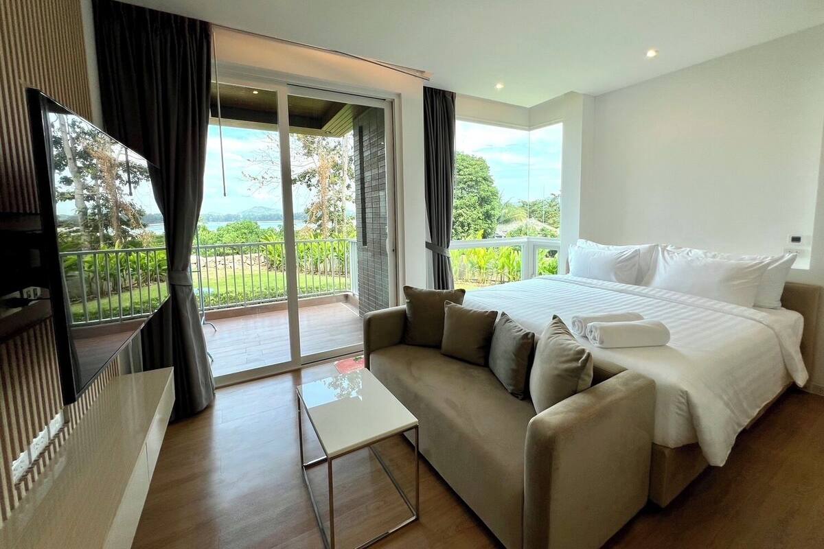 Una habitación de hotel moderna con una cama grande, un sofá, una mesita y un balcón con vistas al exterior.