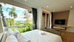 Une chambre d’hôtel dotée d’un grand lit, d’un téléviseur fixé au mur et d’un balcon offrant une vue sur la verdure et un plan d’eau.