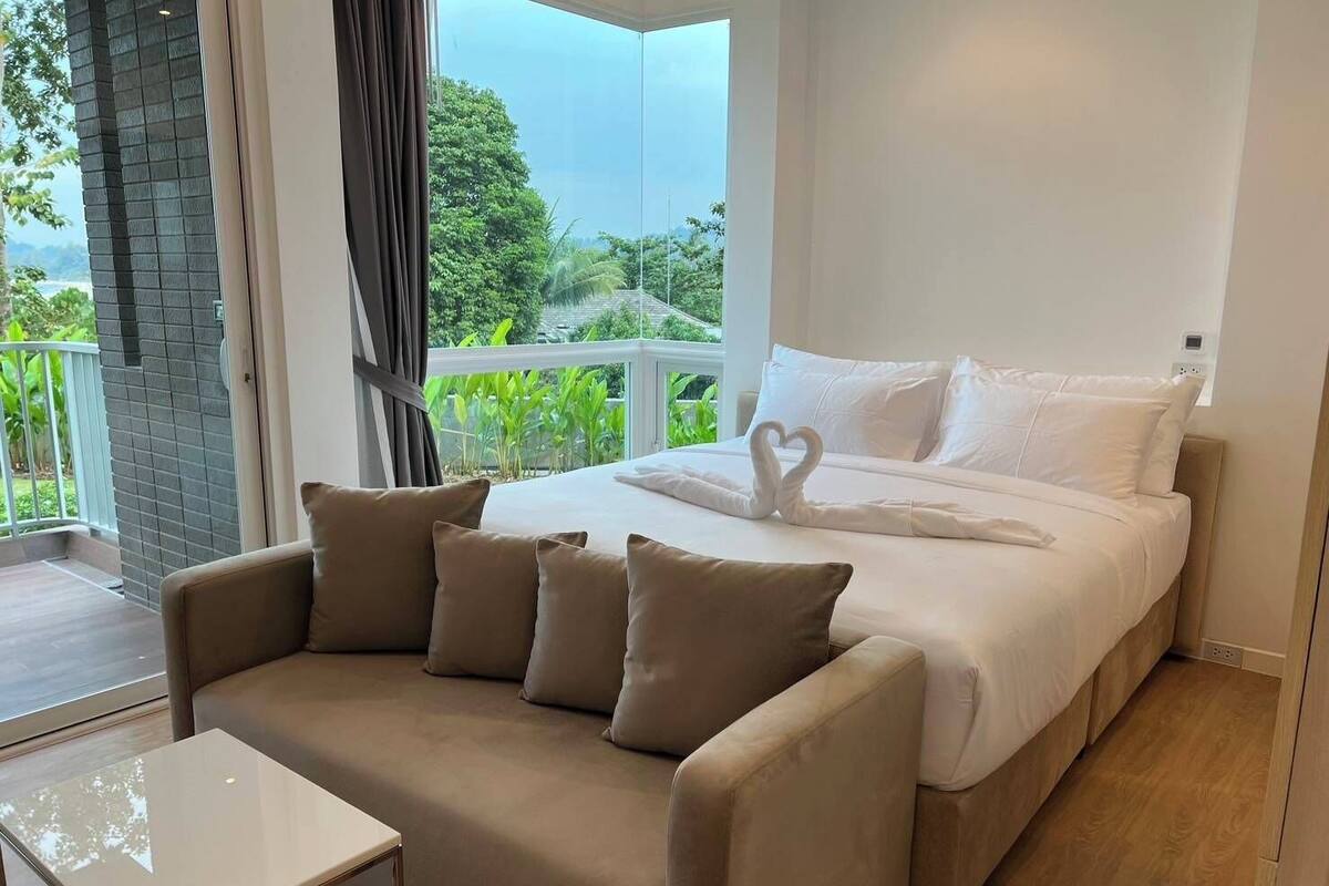 Un dormitorio con cama, sofá y balcón con vistas al verdor.