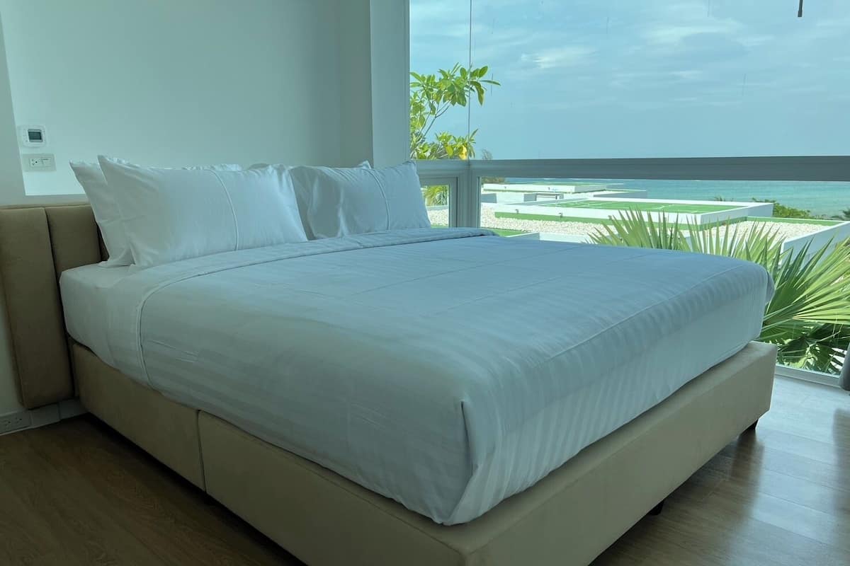 Una cama grande con sábanas blancas en una habitación con vistas al océano.