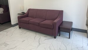 A modern living room with a purple sofa, a small table with a lamp, and a bench.