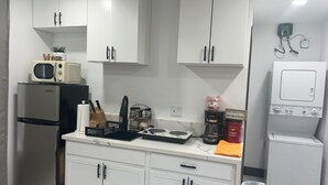 A compact kitchen with white cabinets, a stainless steel refrigerator, a microwave, a coffee maker, and a washing machine.