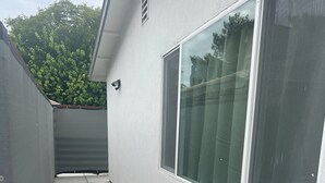 A narrow concrete pathway leading to a building with large windows and a grey fence.