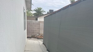 A narrow concrete pathway flanked by a white wall and a dark green fence.