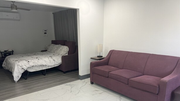 A hotel room with a bed, a purple sofa, a nightstand, and a lamp.