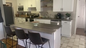 A kitchen with white cabinets, a central island with stools, a microwave, and a coffee maker.