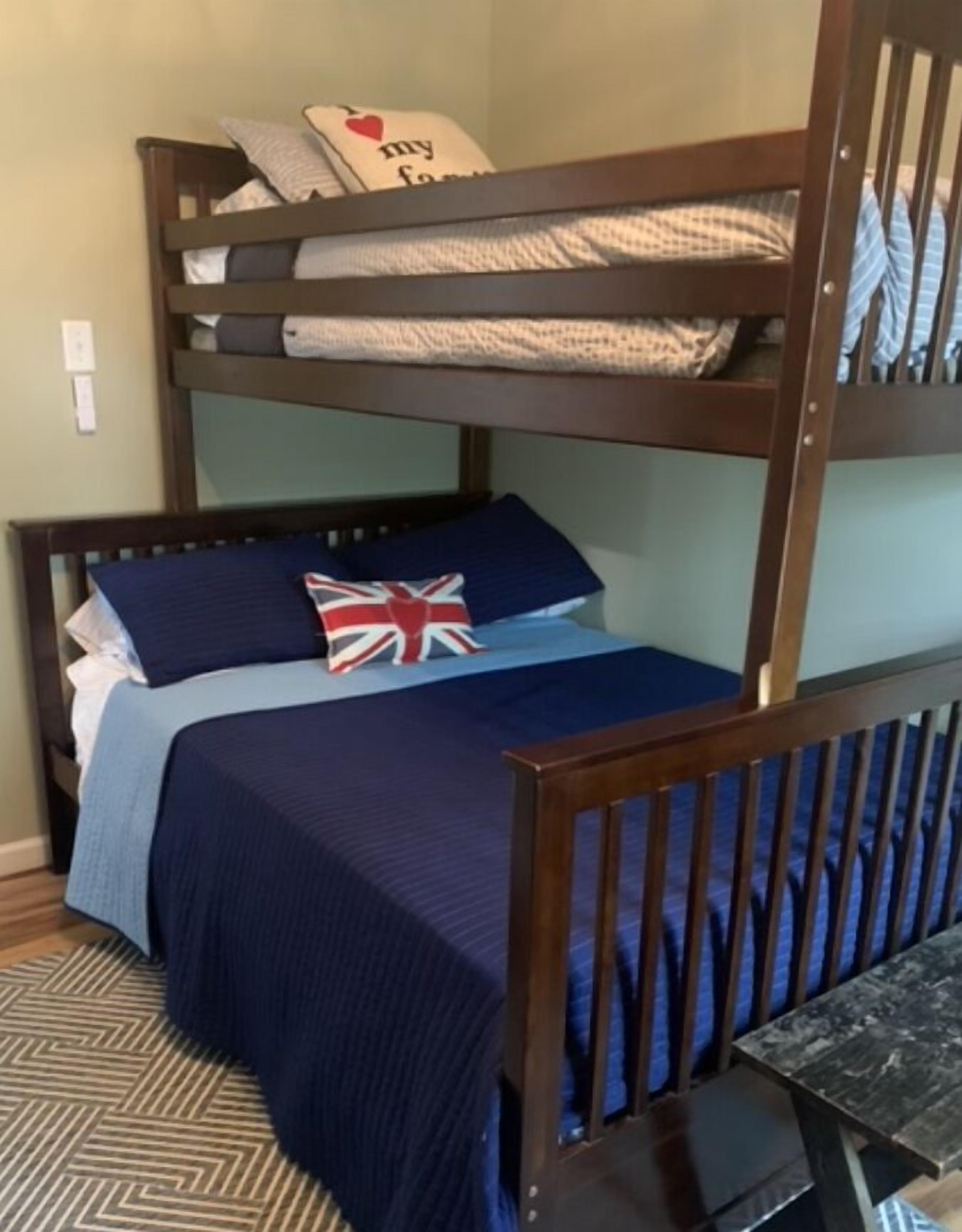 A bunk bed with a blue bedspread and pillows, a small table, and a flag pillow.
