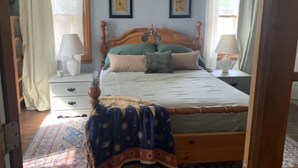 A bedroom with a wooden bed, two nightstands, a bedside lamp, a window with curtains, and a framed picture on the wall.
