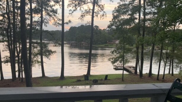 A view of a lake with trees and a dock, a metal table with a candle, and a bench.