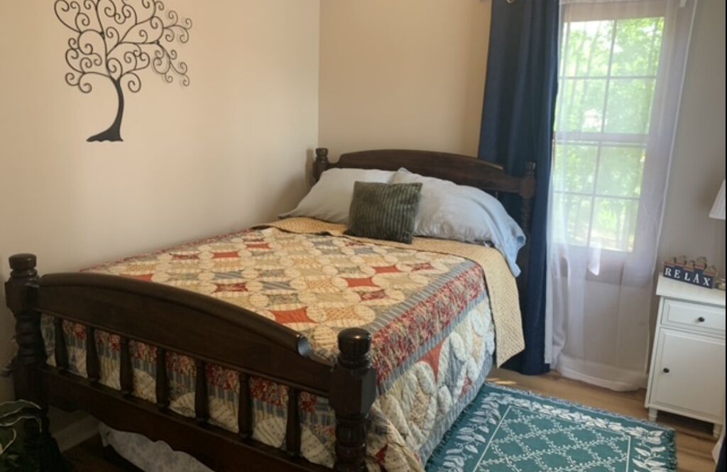 A bedroom with a wooden bed, a quilt, a nightstand, and a window with curtains.