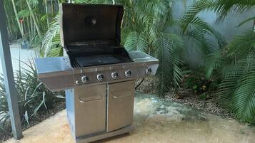 A stainless steel outdoor grill with four burners, a side shelf, and a hinged lid.