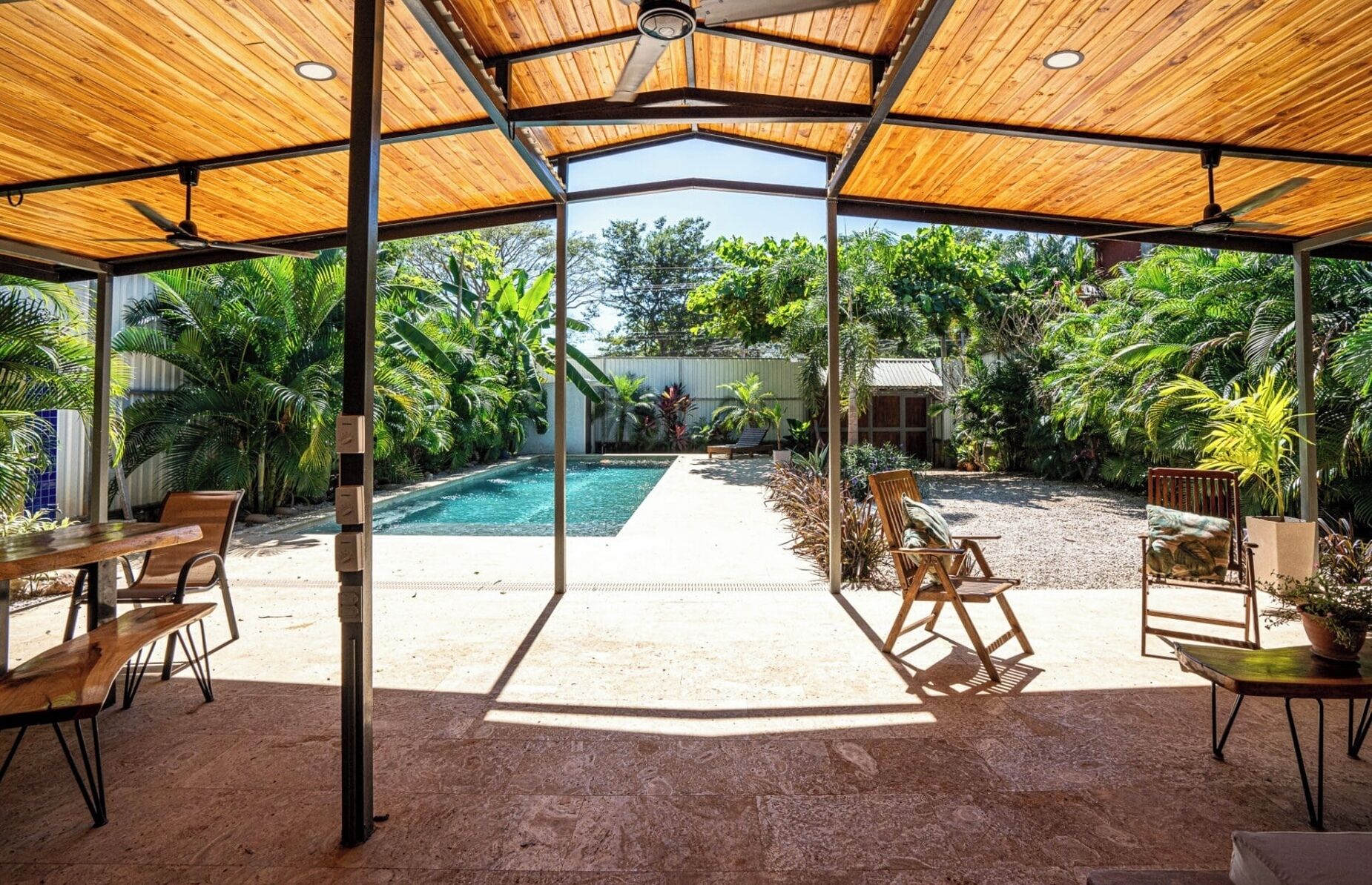 Un espace extérieur abrité comprenant une piscine, des sièges et des plantes tropicales.