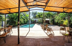 Ein überdachter Außenbereich mit Pool, Sitzgelegenheiten und tropischen Pflanzen.