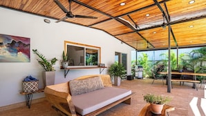 A modern living room with a wooden sofa, a coffee table, and a dining area with outdoor seating. - Lovely 2 bedroom home with large Private salt water pool in beautiful Tamarindo. (Tamarindo)