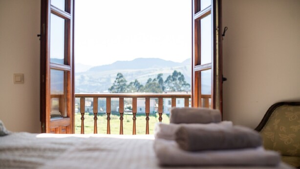 Una camera da letto con un letto, un balcone con ringhiera in legno e vista sulle montagne.