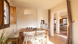 Zona pranzo con tavolo in legno e sedie bianche, lampadario a sospensione e vista sulla cucina.