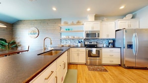 A modern kitchen with white cabinets, stainless steel appliances, a wooden countertop, and a clock on the wall.