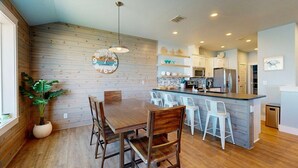A modern kitchen with wooden paneling, a central island with bar stools, and a dining table with chairs.