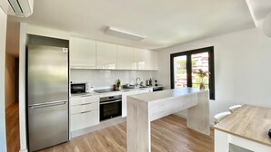 Une cuisine moderne avec des meubles blancs, un réfrigérateur en acier inoxydable et une table à manger en bois.
