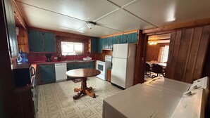 A kitchen with teal cabinets, a white refrigerator, a wooden table, and a patterned floor.