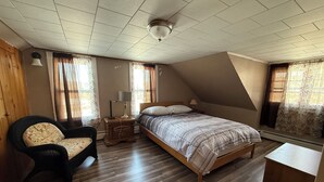 A bedroom with a bed, a chair, a nightstand, a lamp, and a ceiling fan.