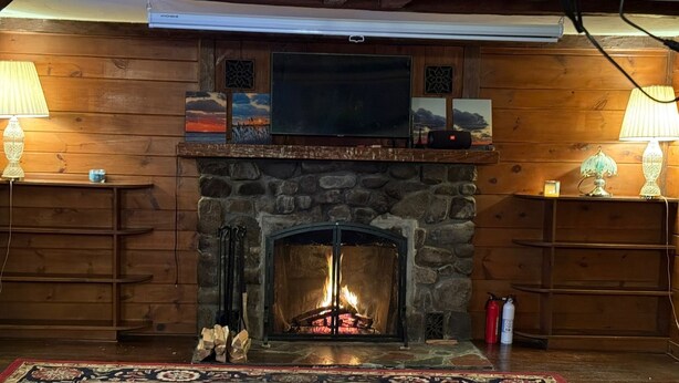 A cozy room with a stone fireplace, wooden walls, and a television above it.