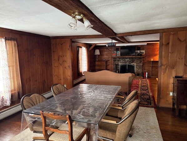 Un intérieur de chalet chaleureux avec une table à manger en bois, des chaises, un canapé recouvert d’un tissu, une cheminée et un téléviseur.