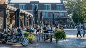Un café al aire libre con mesas y sillas, una motocicleta estacionada cerca y un edificio al fondo.