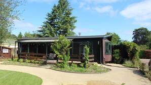 Una casa moderna con un área de estar exterior techada, un árbol grande al frente y un jardín bien cuidado.