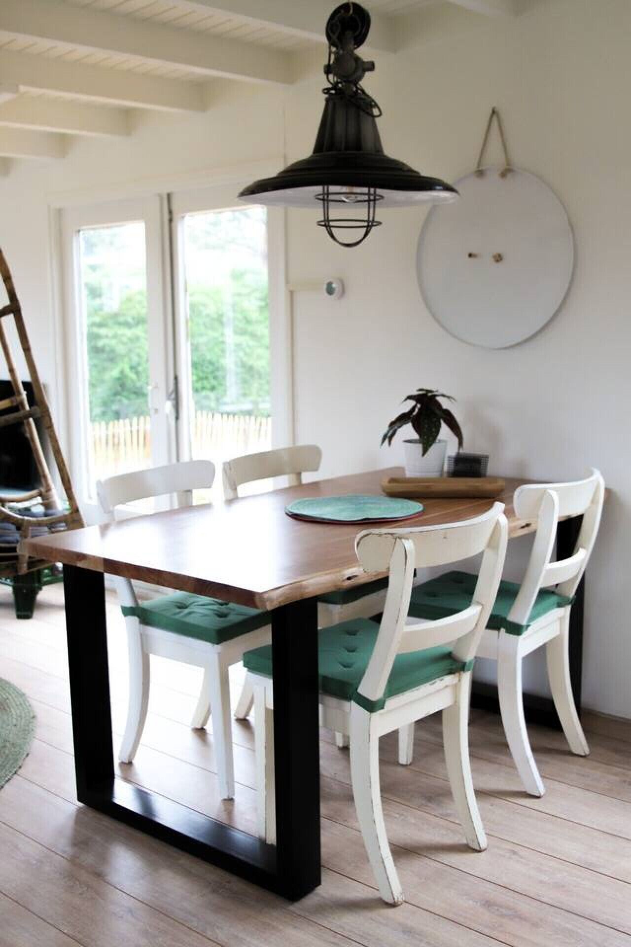 A dining area with a wooden table and white chairs, a black hanging light fixture, and a round white wall decoration.