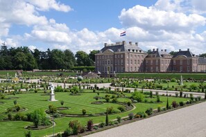 Un grand bâtiment historique, doté d’un jardin à la française devant sa façade, comprenant une fontaine centrale et une disposition paysagère symétrique.