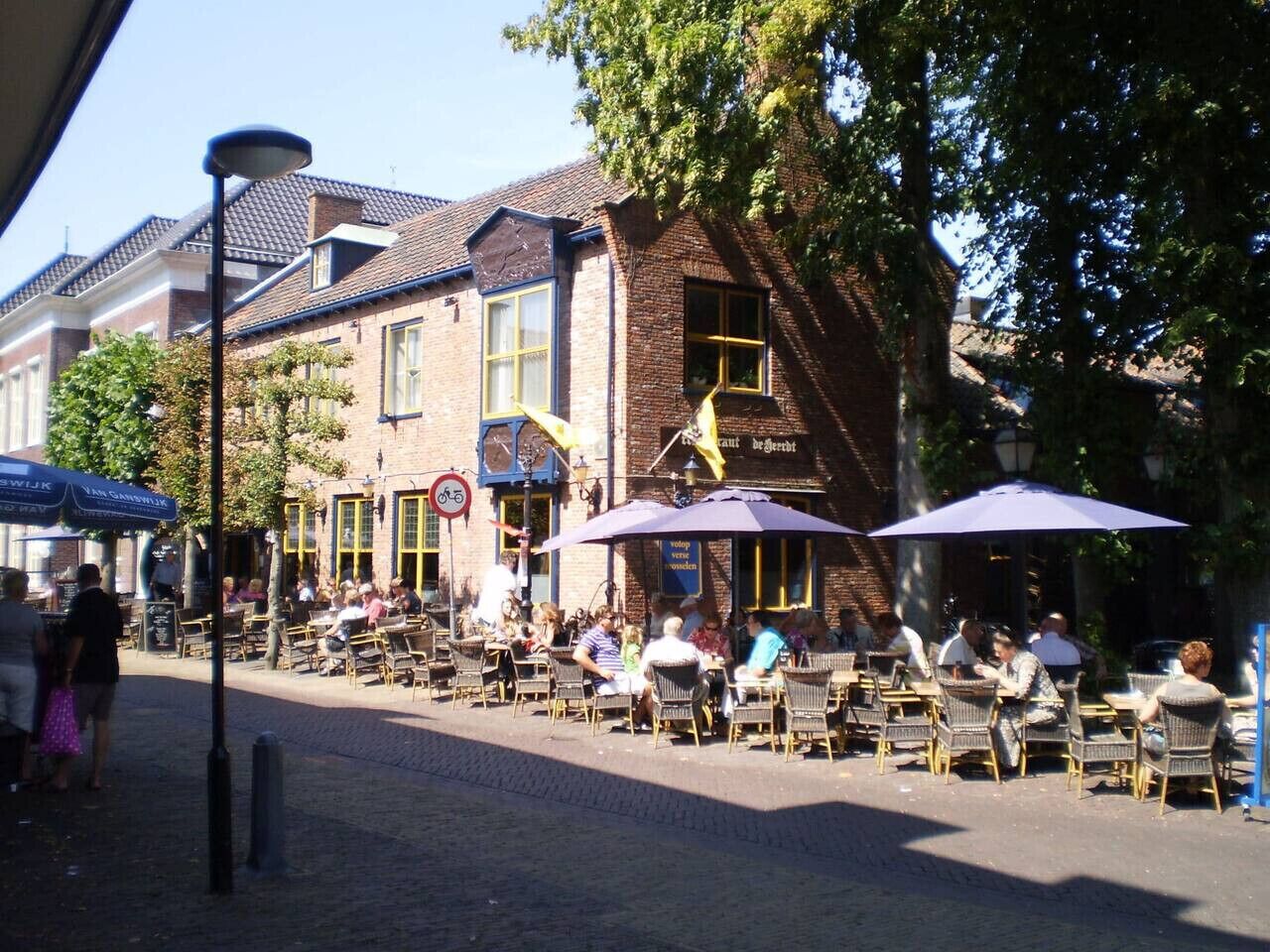 An outdoor café with tables and chairs, a street lamp, and a building with a sign.
