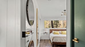 A bedroom with a wooden bed, a bedside table, and a window with a view of trees.