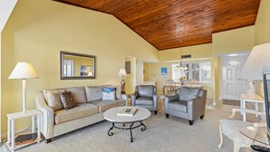 A living room with a wooden ceiling, a beige sofa, two armchairs, a coffee table, and a dining area with a table and chairs. - CP 233 Ocean View Condo - Welcome to Paradise (Fort Pierce)