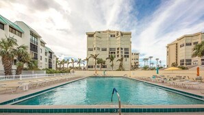 A swimming pool with lounge chairs and palm trees, surrounded by multi-story buildings. - CP 233 Ocean View Condo - Welcome to Paradise (Fort Pierce)