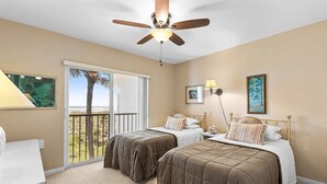 A bedroom with two beds, a ceiling fan, a balcony with a view, and artwork on the walls. - CP 233 Ocean View Condo - Welcome to Paradise (Fort Pierce)