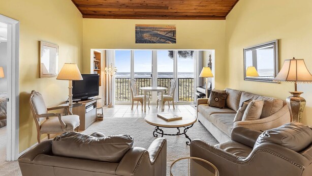 A spacious living room with a wooden ceiling, a television, leather sofas, and a balcony with a view. - CP 233 Ocean View Condo - Welcome to Paradise (Fort Pierce)