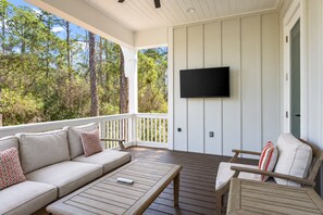 Un área de estar al aire libre techada con un sofá, sillas y un televisor de pantalla plana montado en la pared.
