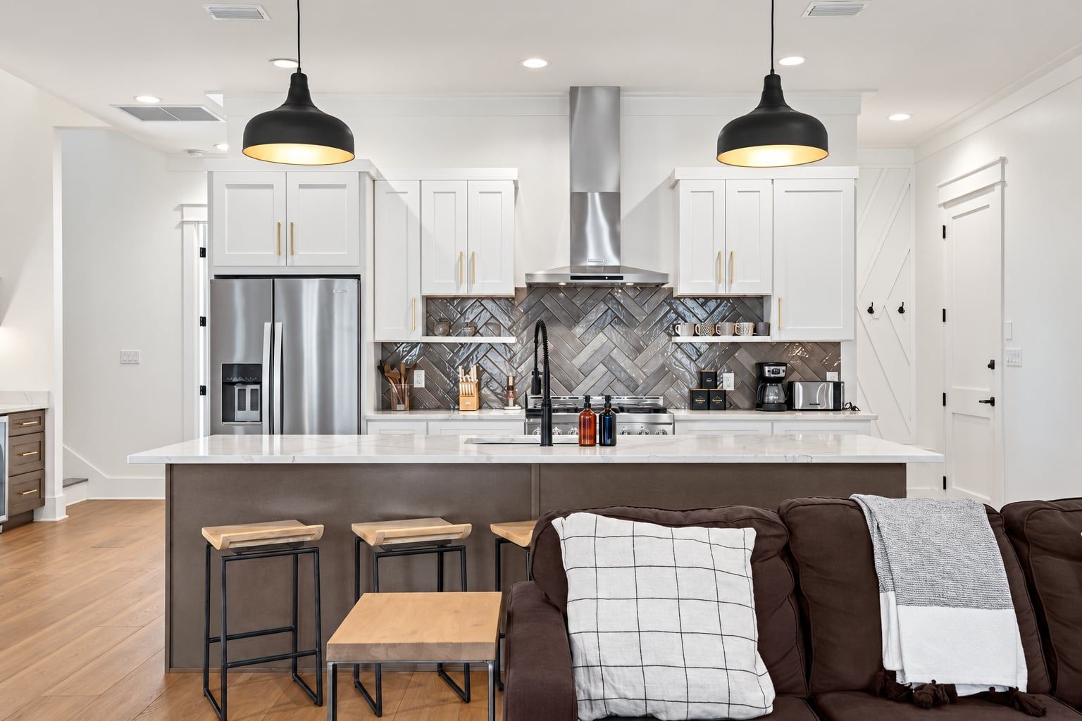 A modern kitchen with a central island, stainless steel appliances, and a herringbone-patterned backsplash.