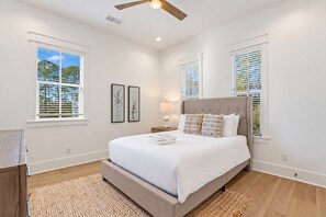 Ein Schlafzimmer mit einem großen Bett, einem Deckenventilator und zwei Fenstern mit Jalousien.