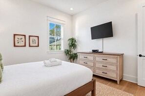 Un dormitorio con una cama, un televisor montado en la pared, un aparador y una ventana con persianas.