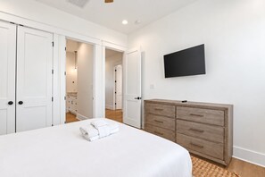 A bedroom with a bed, a dresser, a television on the wall, and a bathroom in the background.