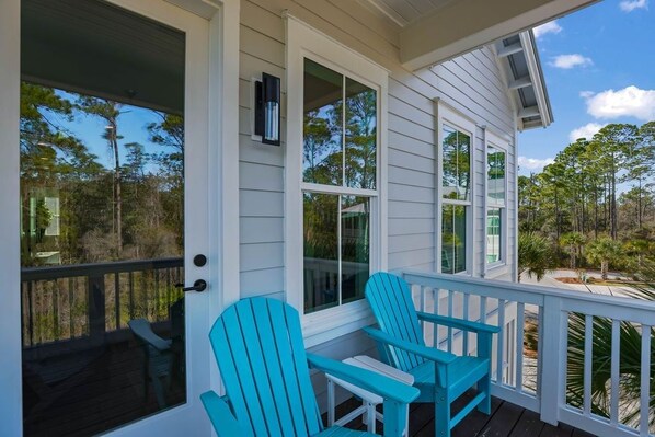 A porch with two chairs, a door, and a window overlooking a wooded area.