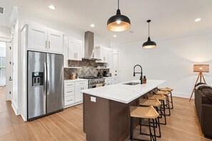 A modern kitchen with white cabinetry, stainless steel appliances, a central island with bar stools, and pendant lighting.