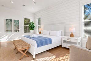 A bedroom with a bed, bedside tables, a lamp, a plant, and artwork on the wall.