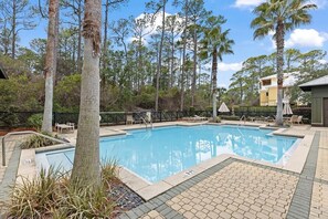 A swimming pool with a tiled deck, surrounded by trees and a building.