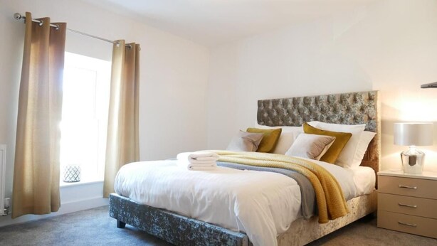 A bedroom with a bed, curtains, a bedside table, and a lamp. - The Courtyard (Ulverston)
