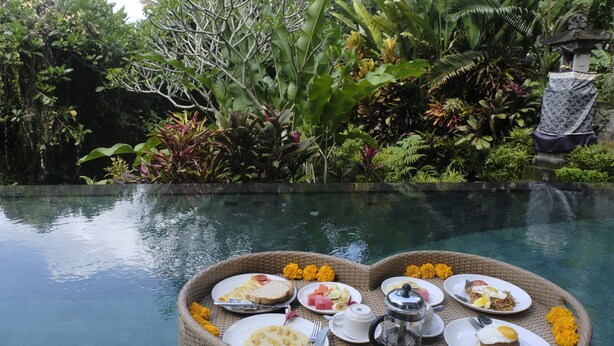 A dining setup by a pool with various dishes and a beverage. - Umah Kemuning Near Central Ubud Bali (Bali)