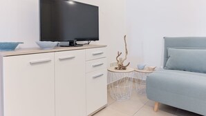 Ein modernes Schlafzimmer mit einem Flachbildfernseher auf einer Holzkommode, einem Bett mit hellblauer Bettwäsche und zwei kleinen, runden Tischen mit Dekoration.